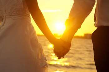 A couple holding hands at sunset on the beach.