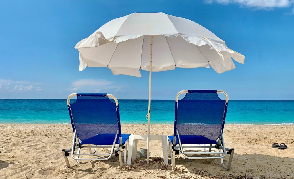 Two lawn chairs under an umbrella on the beach.