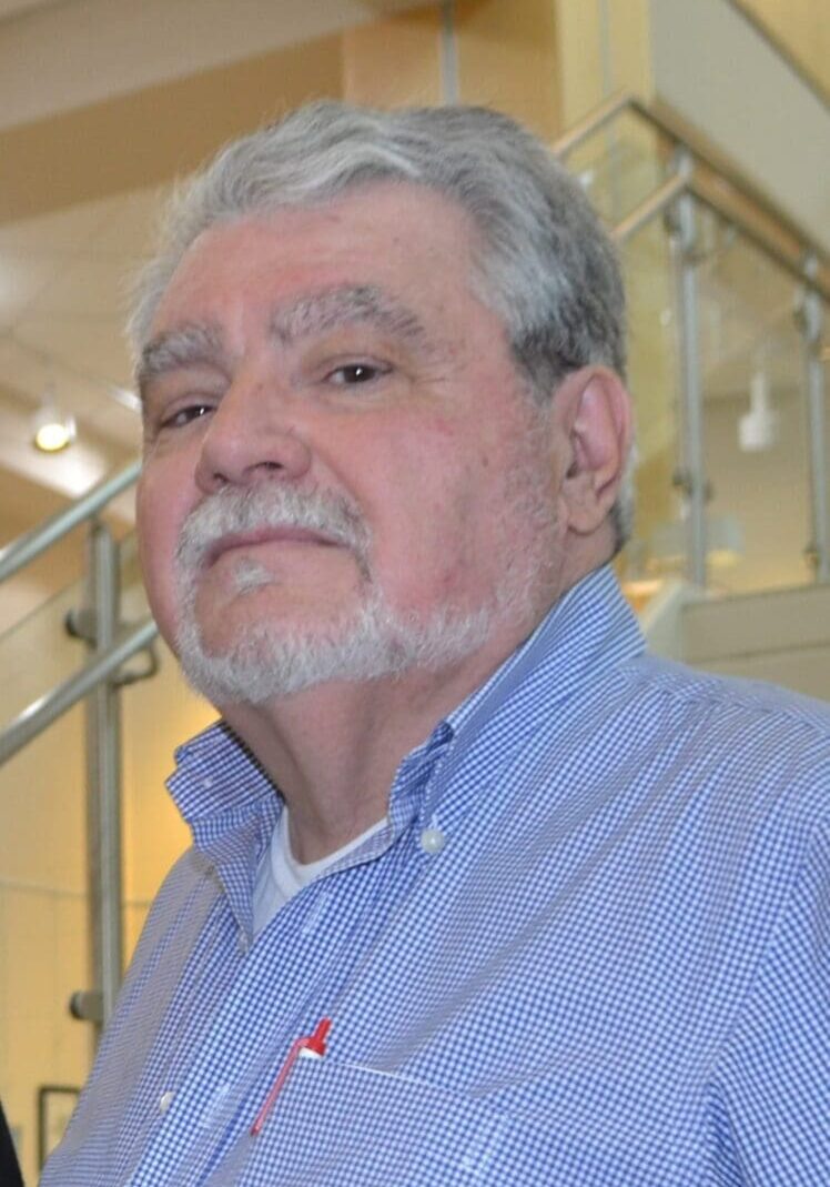 A man with grey hair and beard wearing a blue shirt.